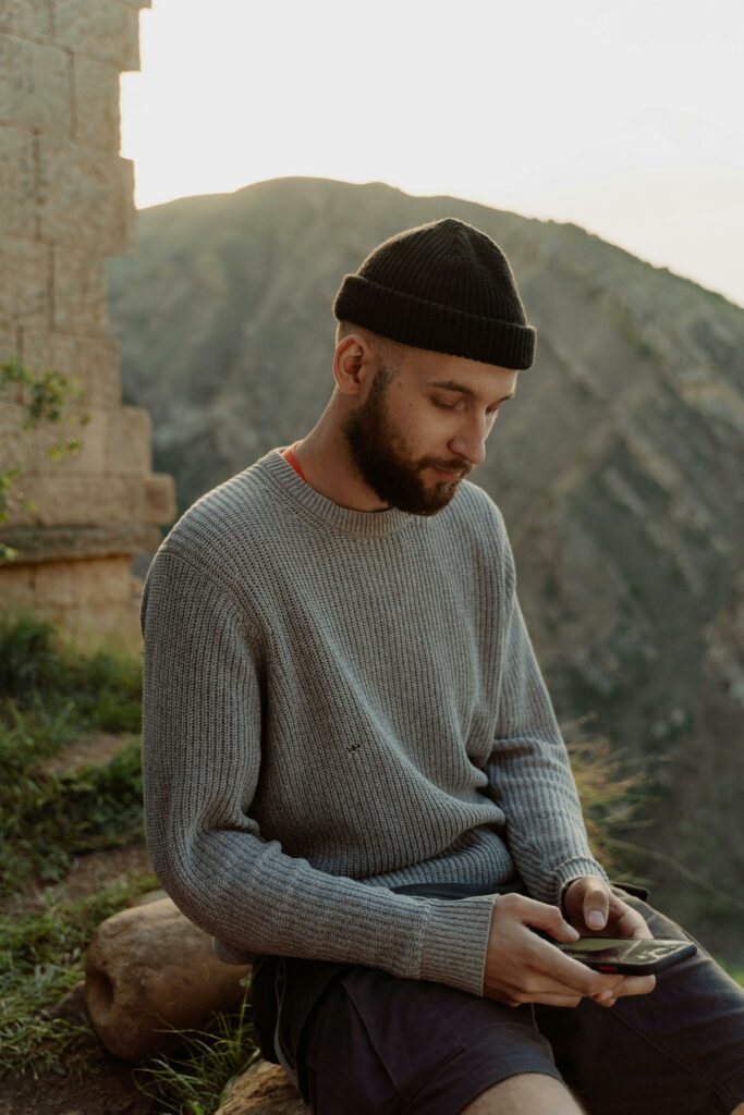 A young man enjoys a leisurely moment outdoors, using his smartphone with mountain views.